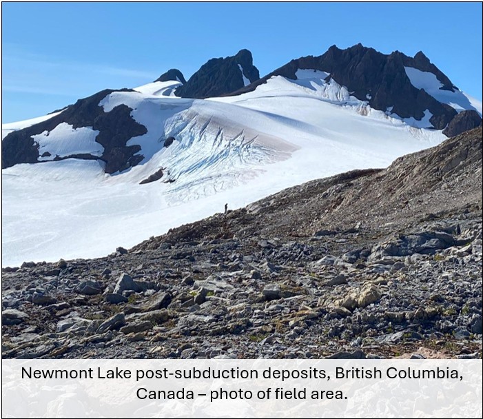 A picture of the Newmont Lake field area for this project - mountains capped with snow, with a geologist standing on a scree slope in the foreground.